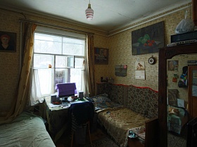 кнопочный телефон, калькулятор и ноутбук на квадратном столе со скатертью у окна с белой гардиной и желтыми шторами в спальне деревянной двухэтажной советской дачи художника с овальной террасой