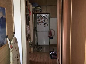 белый холодильник с магнитиками на дверце в углу, большой коричневый шкаф-купе в прихожей с коричневым линолеумом на полу трехкомнатной квартиры