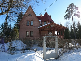 забор из сетки с воротами вокруг неординарного загородного дома с башней на заснеженном участке