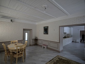 белая кухня из светлой стильной гостиной загородного дома через открытый дверной проем