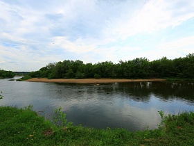 отражение в воде голубого неба с облаками и деревьев вдоль песчанного берега извилистой реки в летнее время