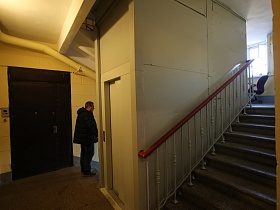 коричневая дверь квартиры, белая дверь лифтовой кабины на лестничной площадке между этажами в жилом многоэтажном доме