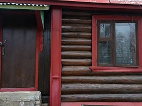 замок на коричневой входной двери с бетонным крыльцом под навесом, окном на бревенчатой стене веранды деревянного домика в деревне