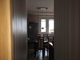 коричневые стулья с бежевой высокой спинкой вокруг темно коричневого обеденного стола у стены кухни с бежевыми полосатыми обоями современной семейной квартиры