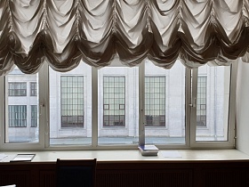широкое белое пластиковое окно с белым полуспущенным ламбрекеном и деревянной декоративной решеткой под подоконником для отопительной батареи на стене в кабинете КГБ СССР