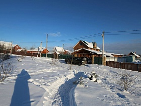 протоптанная дорожка в сугробах белоснежного снега к трех этажному дому в деревне у пруда