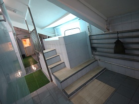 небольшой высокий бассейн, выложенный прямоугольным белым кафелем, на ступенях с металлическим ограждением в просторной комнате с душевыми кабинками