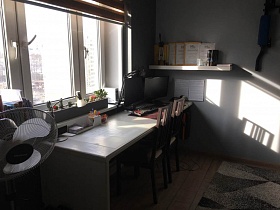 два письменных стола у большого окна с кактусами на подоконнике, грамоты на белой полке в юношеской комнате с серым ковром на полу современной квартиры