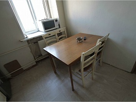 белые стулья со спинкой вокруг прямоугольного коричневого стола у окна с микроволновкой на белом подоконнике светлой кухни сталинской простой квартиры для съемок кино