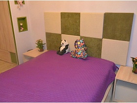 комнатные цветы на тумбочках у кровати с мягкими игрушками на фиолетовом покрывале детской комнаты