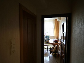 открытая дверь в кухню с овальным обеденным деревянным столом на ножке у стены