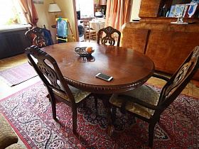 резные деревянные спинки старинных стульев у круглого стола в центре гостиной квартиры эпохи СССР
