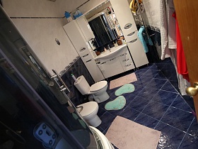 белый шкаф с зеркалом и раковиной, санузел, полотенцесушитель,душевой бокс , дорожки на полу с синей плиткой в ванной комнате семейной дачи с видом на город