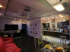 общий вид сиреневой гостиной и смежной кухни с темной мебельной стенкой на подиуме квартиры студии молодой семьи в современном стиле