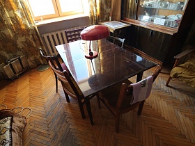 стулья со спинкой вокруг раздвижного полированного стола с красной настольной лампой в гостиной эпохи СССР