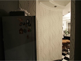 холодильник с магнитами и черной коробкой у белой стены с разводами в коридоре квартиры с выходом на крышу магазина