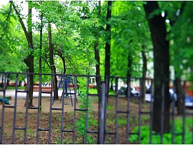 детская игровая площадка за высоким серым металлическим забором в старом дворе трехэтажного дома