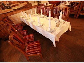 резные спинки стульев из натурального дерева с красной полосатой обивкой вокруг сервированного банкетного стола с белоснежной скатертью в уютном зале ресторана с кавказким интерьером