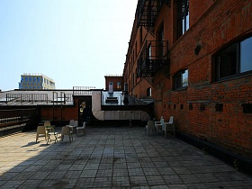 открытая терраса кафе на крыше за черным металлическим забором БЦ с балконами на стене из красного кирпича