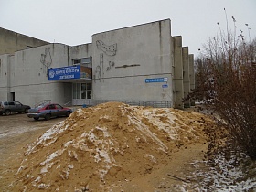 гора песка на территории перед высоким панельным зданием ДК СССР с синими вывесками на его стенах