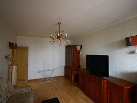 люстра, стилизованная под свечи, телевизор на мебельной стенке в светлой гостиной актерской трехкомнатной квартиры