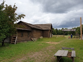 длинный деревянный дом с приставными лестницами к дверям на просторном дворе за открытым деревянным забором в русской деревне для съемок кино