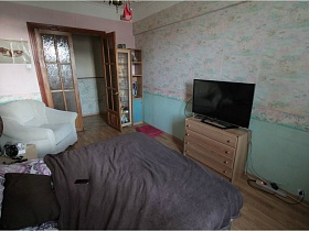 большая кровать, белое мягкое кресло, телевизор на комоде в спальной комнате с двухстворчатыми дверьми со стеклянными вставками сталинской квартиры 90-ых годов