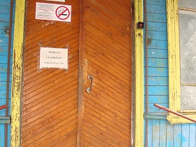 лампа дневного света и знак "инвалид" над входными деревянными дверьми со старой желтой краской на лутке и оконных рамах деревянной больницы