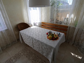 фрукты на широком блюде, сахарница и салфетки на длинном столе с белой скатертью у окон светлой кухни семейной уютной дачи с частиным недостроем