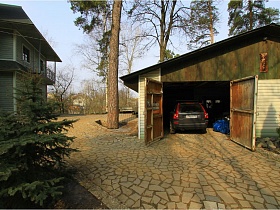 машина в гараже с открытыми воротами на просторном ухоженном участке с дорожками, выложенными диким камнем