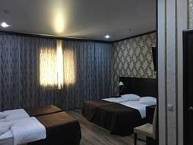 зашторенные окна комфортабельного номера современной гостиницы на четыре человека с аккуратно заправленными кроватями, цветочными обоями на стенах и подвесным потолком