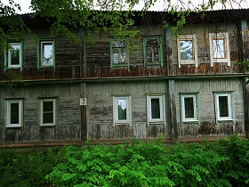 старинный двухэтажный деревянный дом под номером 7 с пластиковыми окнами жилых квартир среди высокой зеленой травы в старом Ногинске
