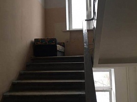 диванчик на площадке лестничного пролета с бетонными ступенями и металлическими перилами подъезда жилого дома