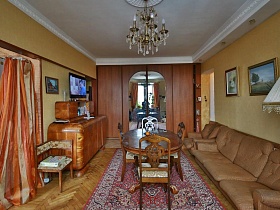 люстра, стилизованная под свечи на белом потолке, большой шкаф для одежды с зеркальными центральными дверцами , мягкая коричневая мебель в гостиной трехкомнатной квартиры времен СССР