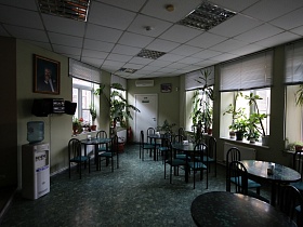 общий вид уютного офисного кафе с круглыми черными столиками на сером мраморном полу, комнатными цветами на белых подоконниках окон, музыкальным центром на стене и белым потолком