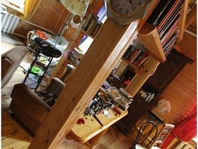 круглые часы на деревянной балке с полками для книг, между двумя отдельными зонами в деревянной дачи музканта