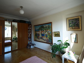 высокий комнатный цветок в вазоне, белый столик у стены с цветочными картинами и картиной с изображением Гагарина в окружении пионеров в светлой спальне квартиры художника