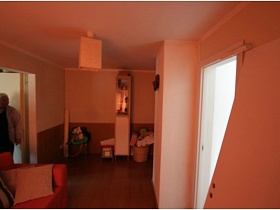 плетенная корзина с вещами, узкий пинал, стул у стены проходной комнаты с коричневыми панелями на стенах