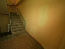 ступени лестницы с перилами у непрокрашенной стены между этажами в подъезде многоэтажного жилого дома