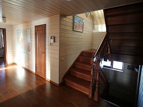 картины на светлых стенах просторного холла с деревянной лестницей в современном трехэтажном доме