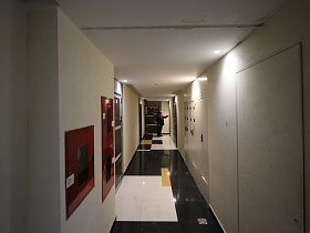 щитовая на светлых стенах длинного коридора на этаже с большой квадратной плиткой на полу и входными дверьми в жилые квартиры современного жилого дома в новостройках