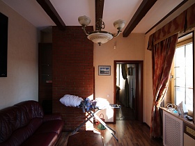 утюг на деревянном подоконнике окна с коричневыми шторами, белье на гладильной доске у кирпичного дымохода для камина в кабинете загородного дома с башней