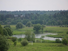 белые футбольные ворота на зеленой поляне у водной глади реки с изгибом в живописном месте