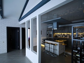серый холодильник, серая мебельная стенка, вытяжка над обеденным столом со встроенной газовой плитой и барными стульями вокруг в зоне кухни загородной скандинавской дачи