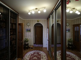 часы, картина на стене и цветы в вазе у арочного проема двери прихожей в большой квартире врача