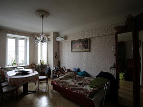 картина над разложенным диваном, гладильная доска с вещами у шкафа с зеркальными дверцами в гостиной квартиры сталинки