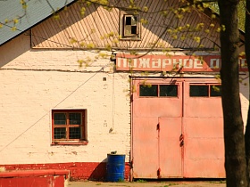 вывеска - Пожарное депо на розовом одноэтажном здании с небольшим окном с решеткой и большими железными воротами Пожарной части ДФ