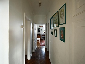 длинный белый коридор с картинами в зеленых рамках на стене