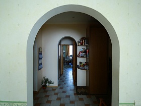 обеденный стол на кухне через арочные дверные проемы прихожей и гостиной в простой большой квартире на втором этаже жилого дома в Марьино