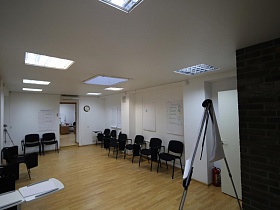 черные мягкие кресла вдоль стены, с окнами и освещением на белом потолке рабочей комнаты офиса